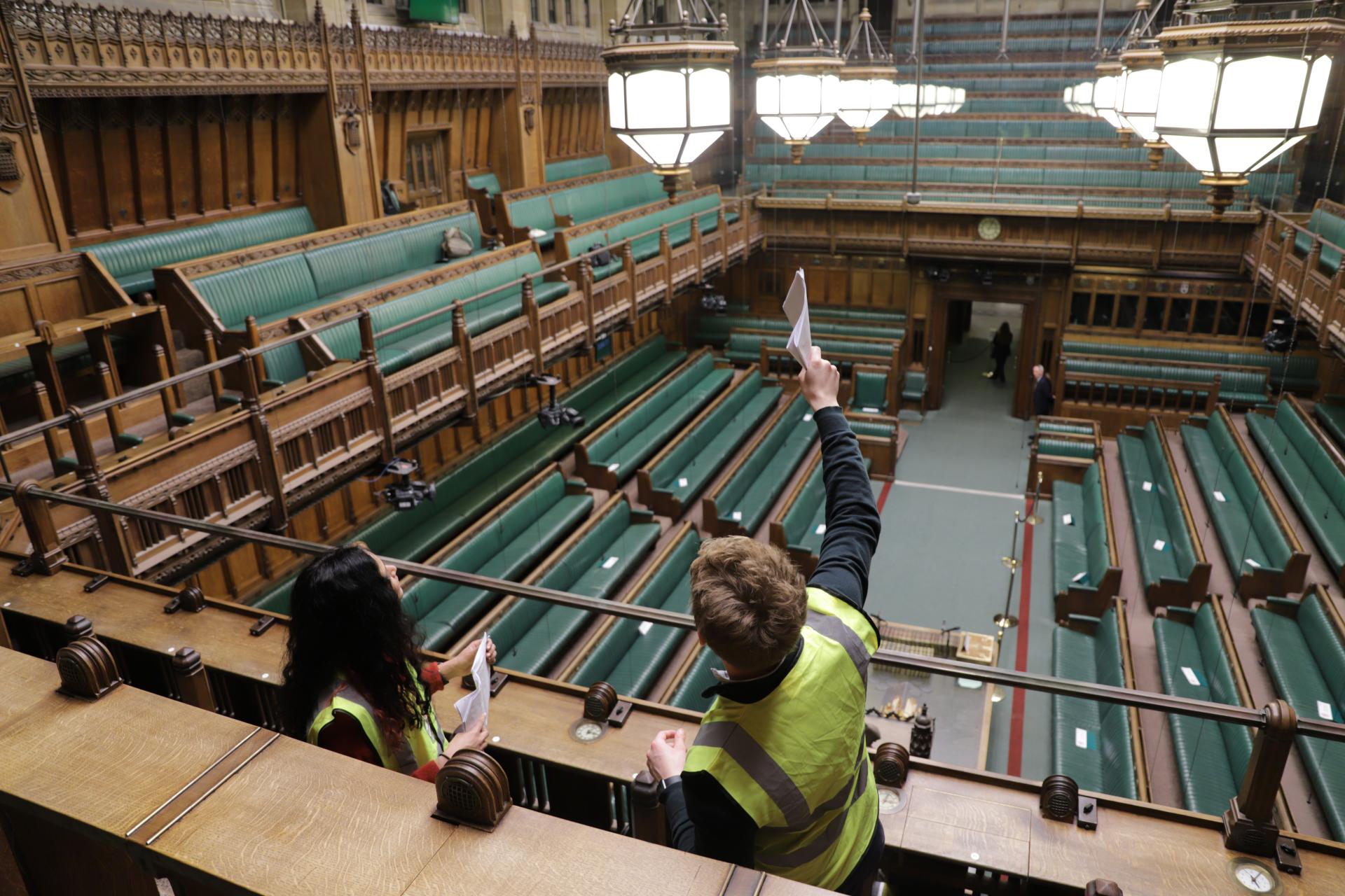 2 people in high vis jackets look up at the ceiling of the House of Commons